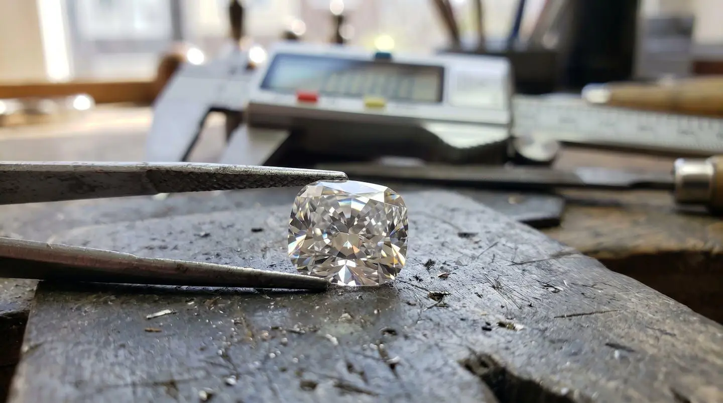 Gros plan sur une main tenant délicatement une rondelle facettée translucide en quartz rose, avec un pied à coulisse numérique visible en arrière-plan flouté, lumière naturelle latérale créant des reflets dans les facettes