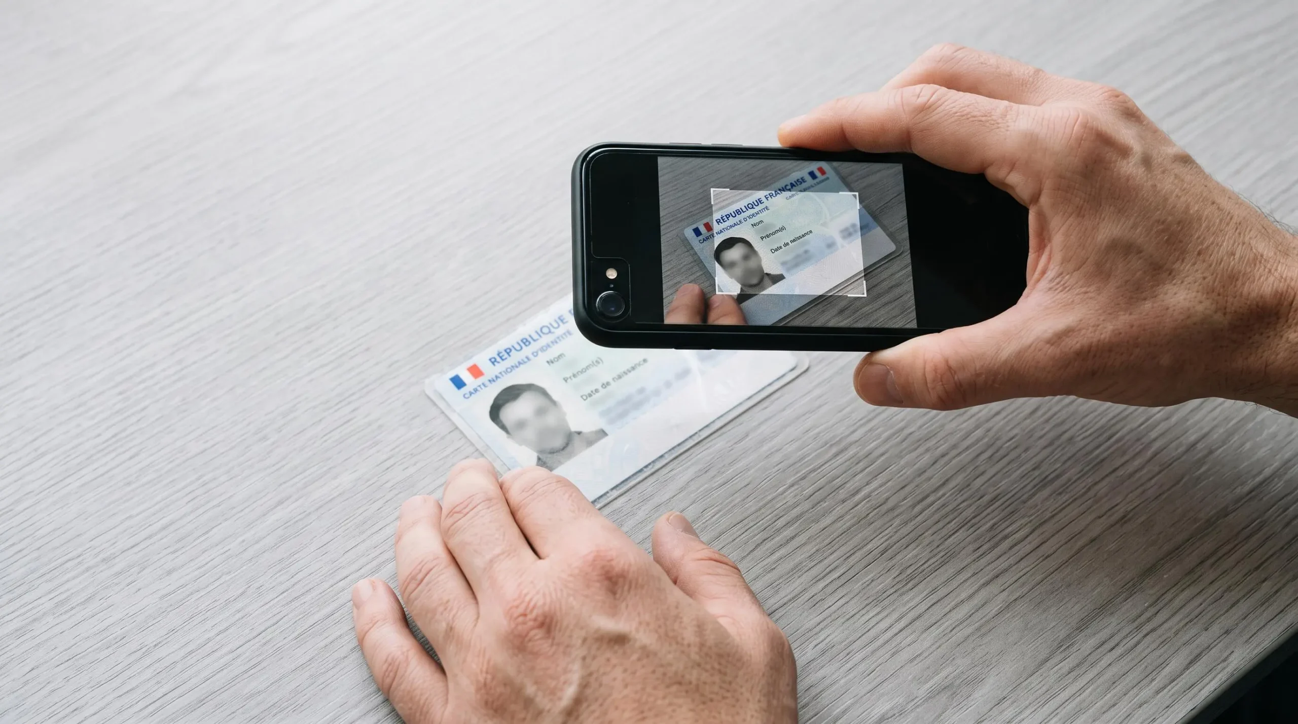 Mains photographiant une carte d'identité française avec un smartphone pour la vérification d'ouverture de compte bancaire en ligne